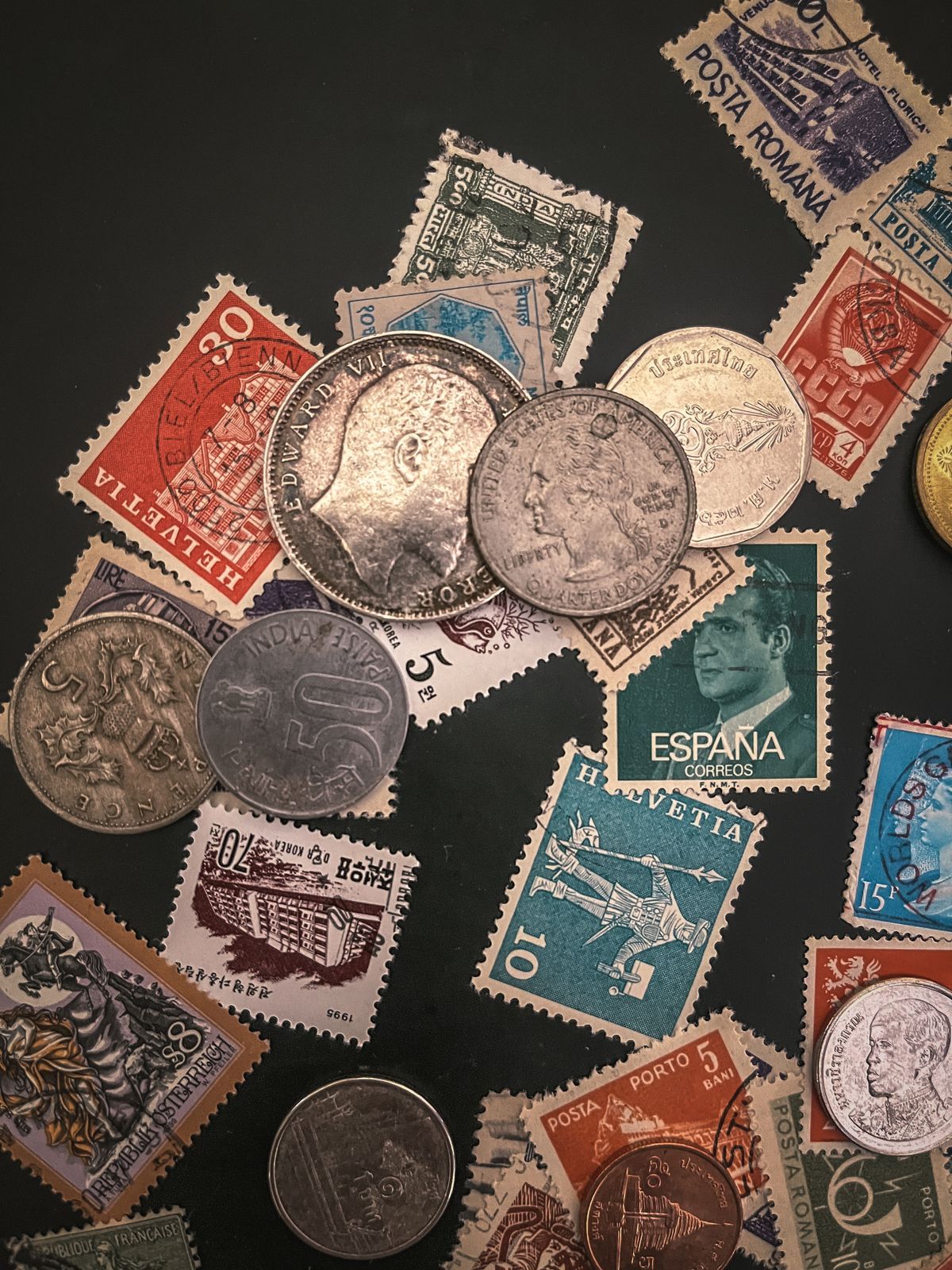Pièces de monnaie et timbres colorés disposés sur un fond sombre.