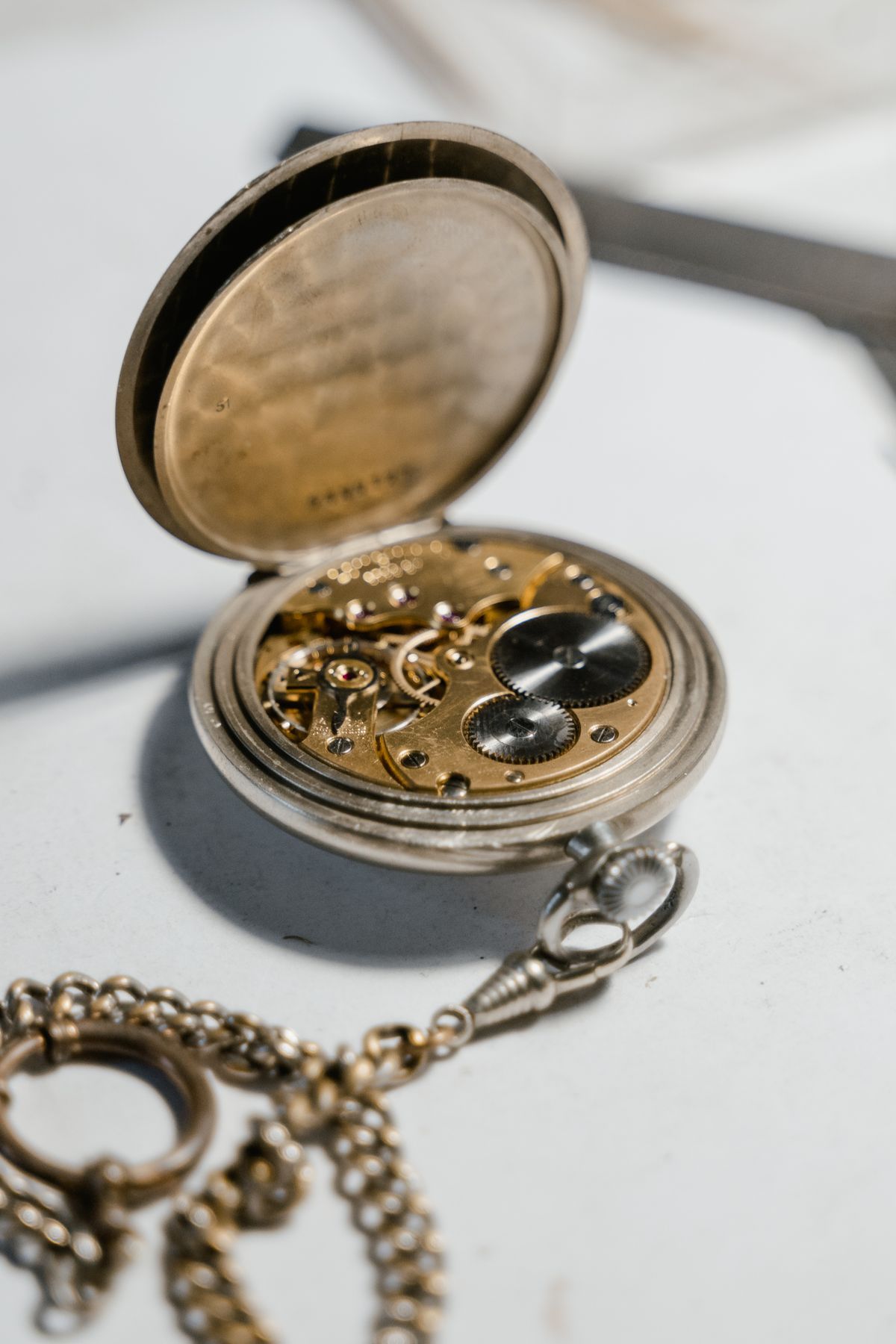 Montre de poche ouverte, rouages apparents et chaîne sur une surface claire.